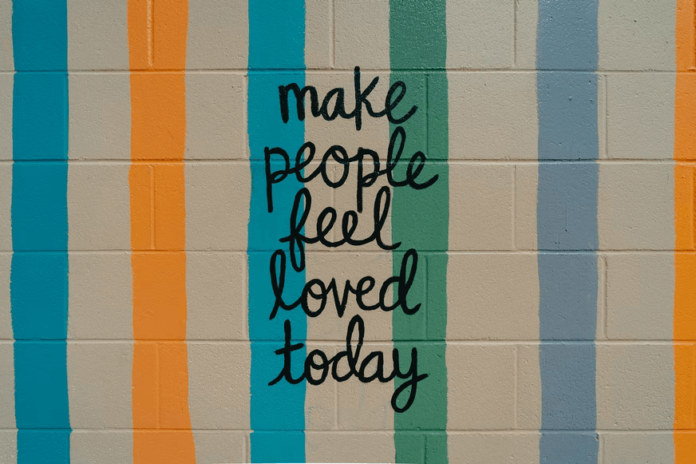 A cinderblock wall painted with cheerful colors and a handwritten message that says "make people feel loved today"