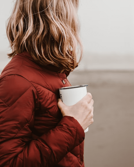 A bundled up woman holding a tumbler with a warm drink.